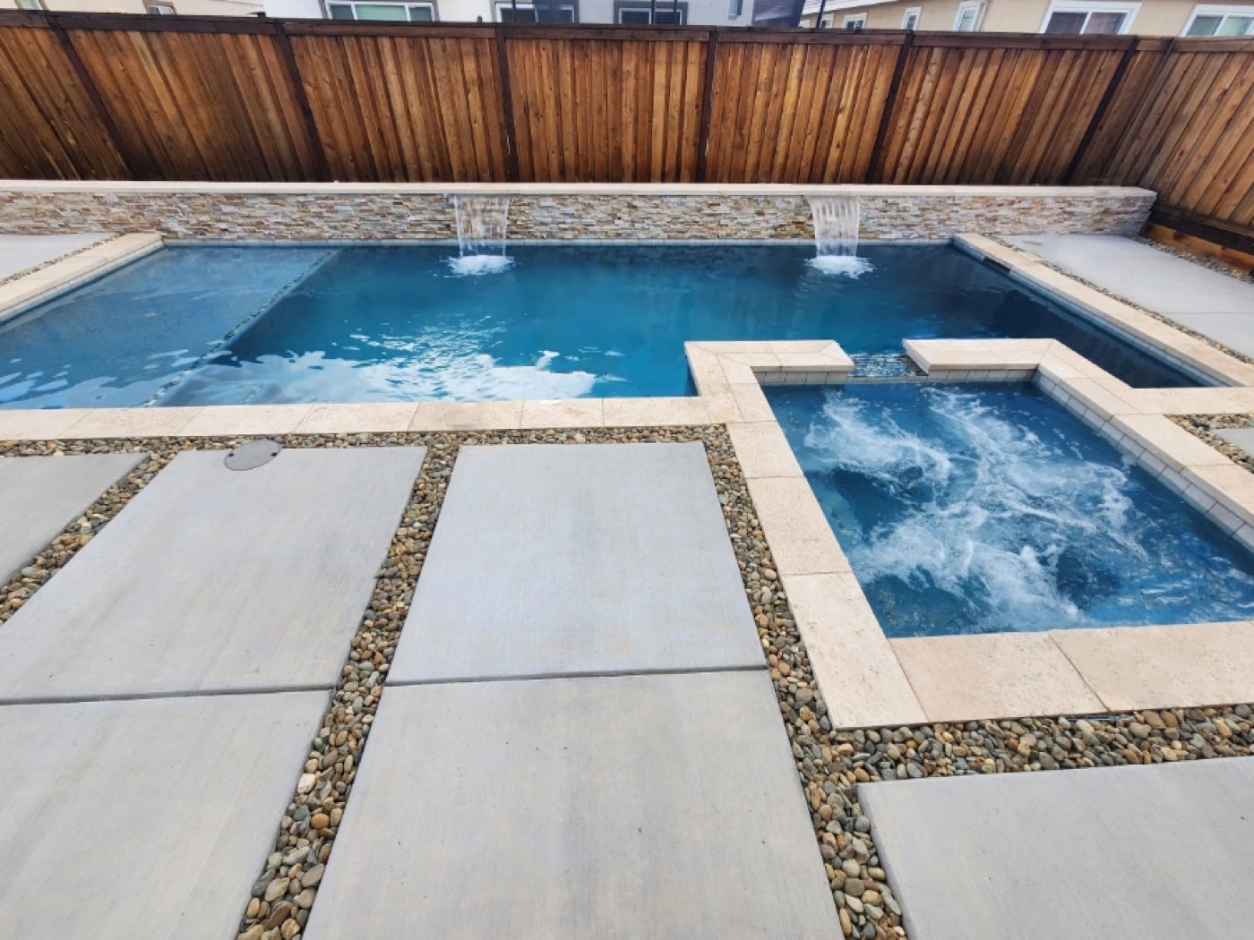 Rectangular shaped pool and spa and raised wall with two sheer descent water features and travertine stone coping.