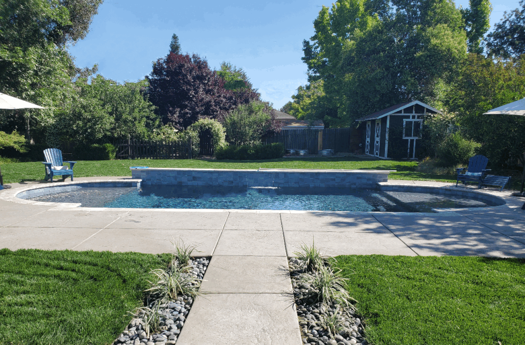 Concrete walkway leading to custom backyard pool installation.