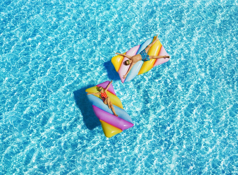 Two children on colorful striped inflatable floats in swimming pool during the day
