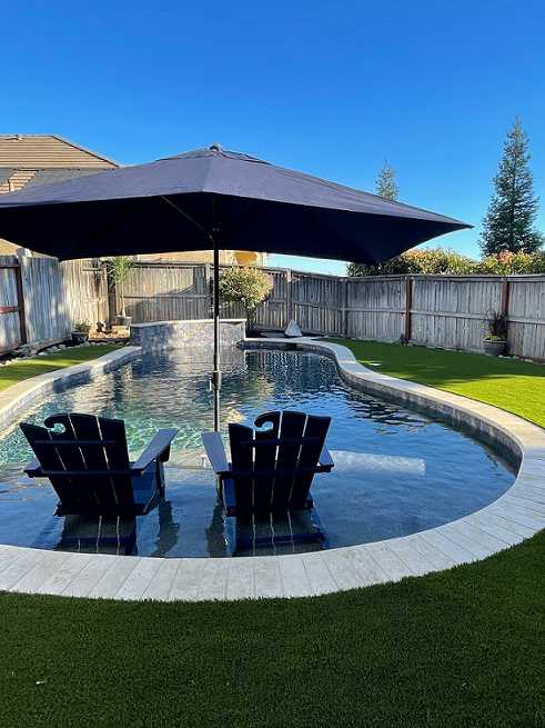Finished freeform shaped pool matching the rendering, with raised bond beam, sheer descent water feature, and patio seating