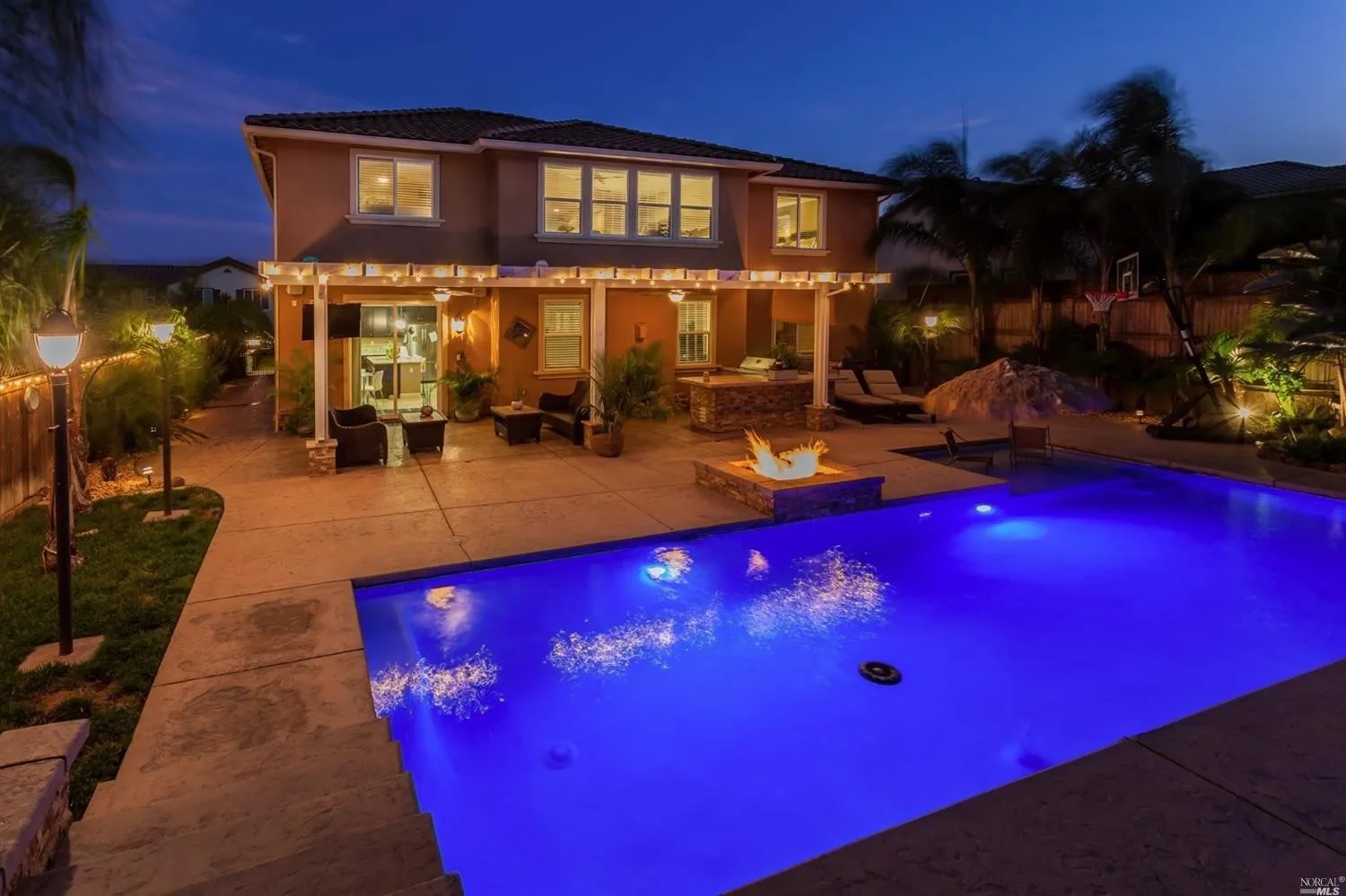 Rectangular shaped pool with a large Cabo shelf and raised fire pit in the evening.