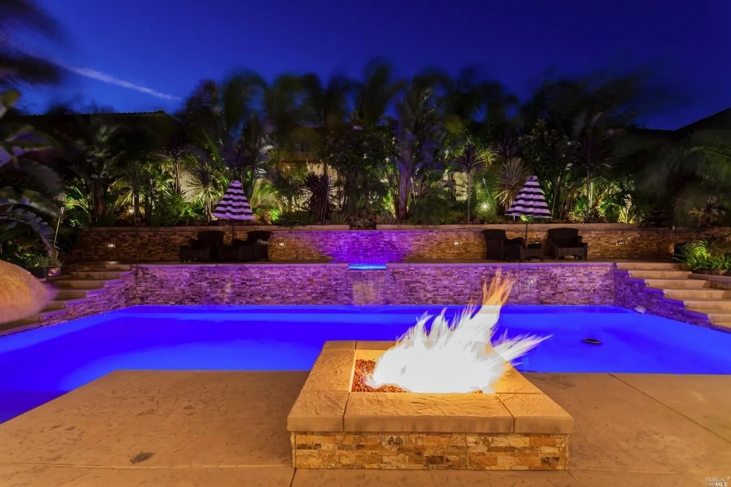 Rectangular shaped pool with a raised walls with a spa and a raised fire pit at dusk.