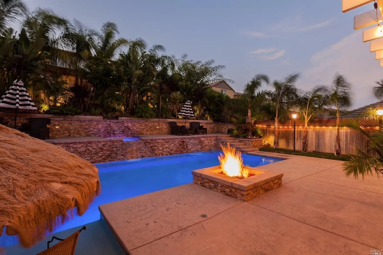 Rectangular shaped pool with a raised walls with a spa and a raised fire pit at dusk.