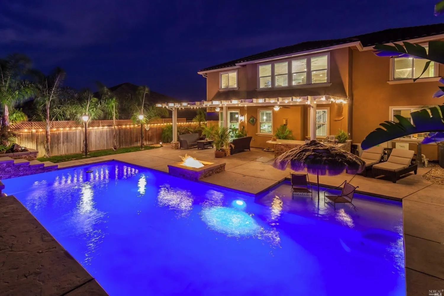 Rectangular shaped pool with a large Cabo shelf and raised fire pit in the evening.