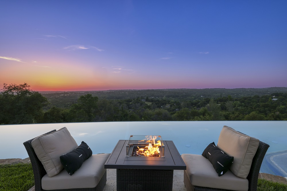 Infinity edge pool with a fire table and chairs at sunset.