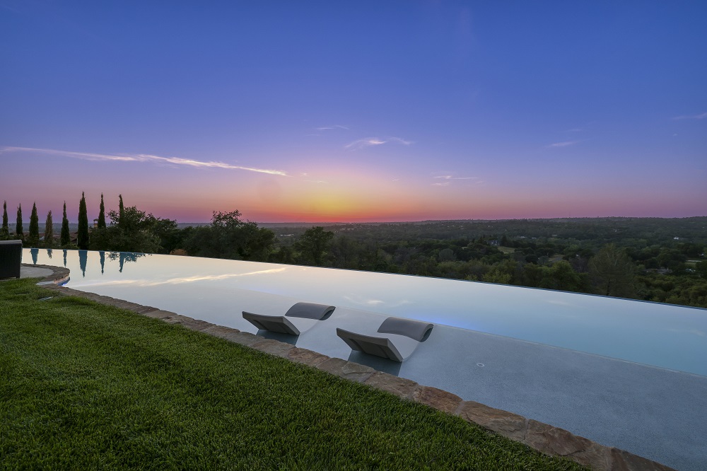 Long curved infinity edge pool with a large Cabo shelf with Lounge Ledger chaises sunset.