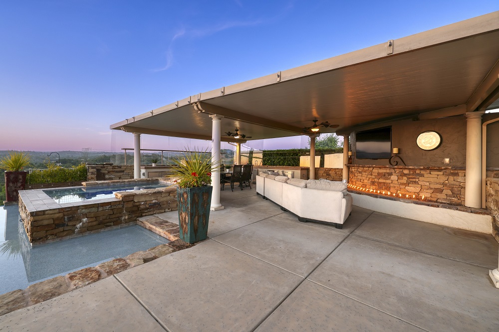 Raised spa with ledger stone and large built in kitchen area with TV and couch at sunset.