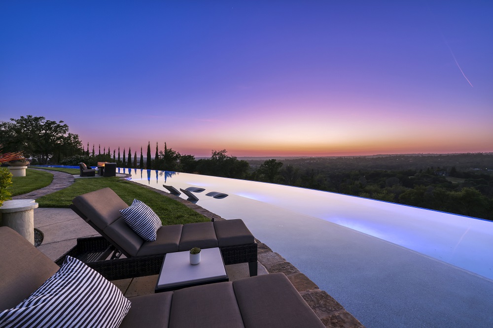 Long curved infinity edge pool with raised spa and long Cabo shelf and chaise lounges at sunset