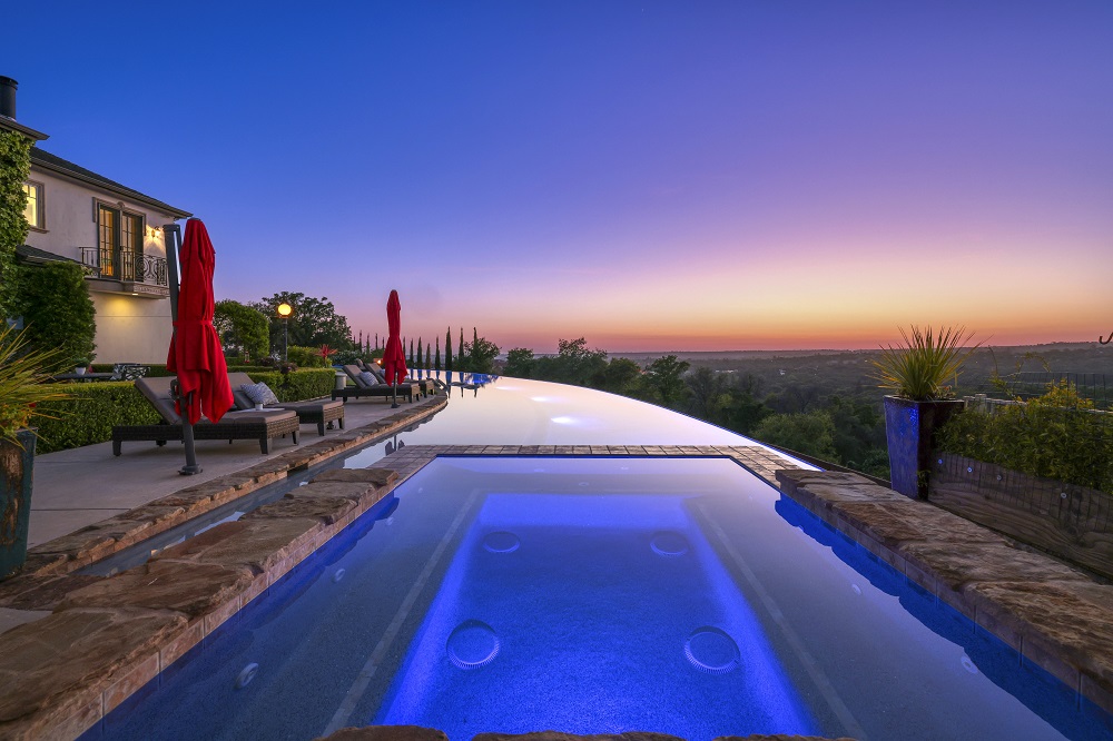 Raised spa connected to a long curved infinity edge pool at sunset.