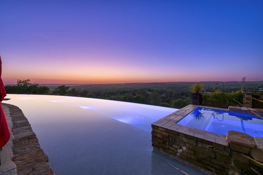 Long curved infinity edge pool with raised spa and long Cabo shelf at sunset