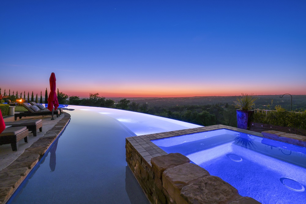 Long curved infinity edge pool with raised spa and long Cabo shelf at sunset