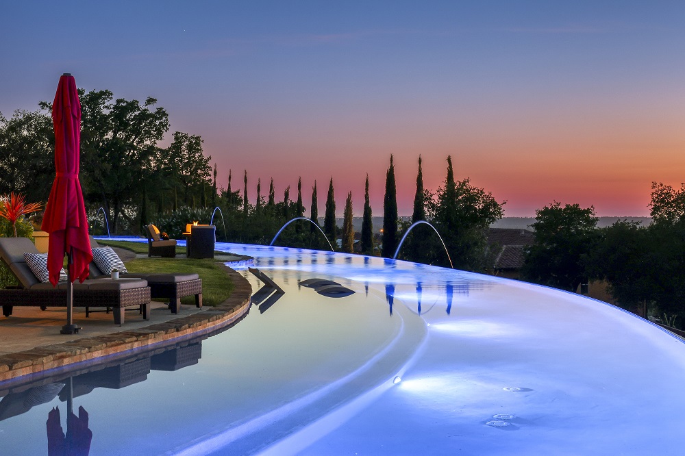 Large curved infinity edge pool with laminars and a fire pit in the evening.