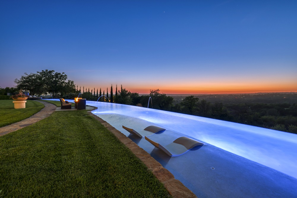 Long curved infinity edge pool with laminars, large Cabo shelf with Lounge Ledger chaises and fire pit at sunset.
