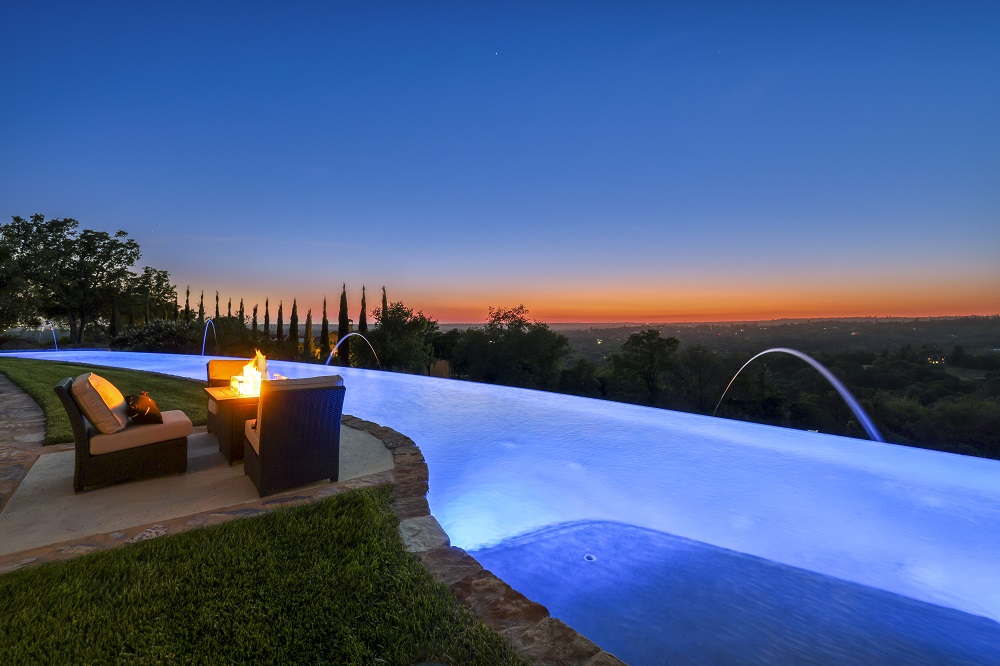 Long curved infinity edge pool with laminars and fire pit at sunset