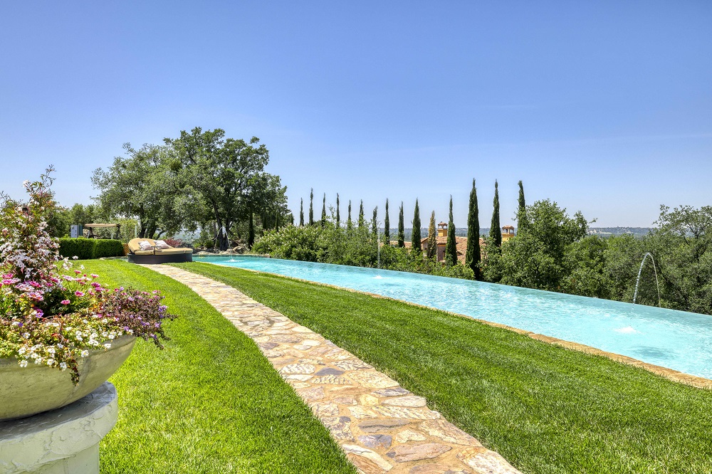 Large curved infinity edge pool with laminars and a grassy area with flagstone walkway.