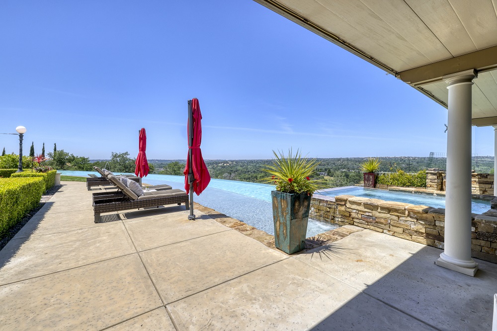 Raised spa with ledgerstone that is spilling over into to a long curved infinity edge pool during the day.