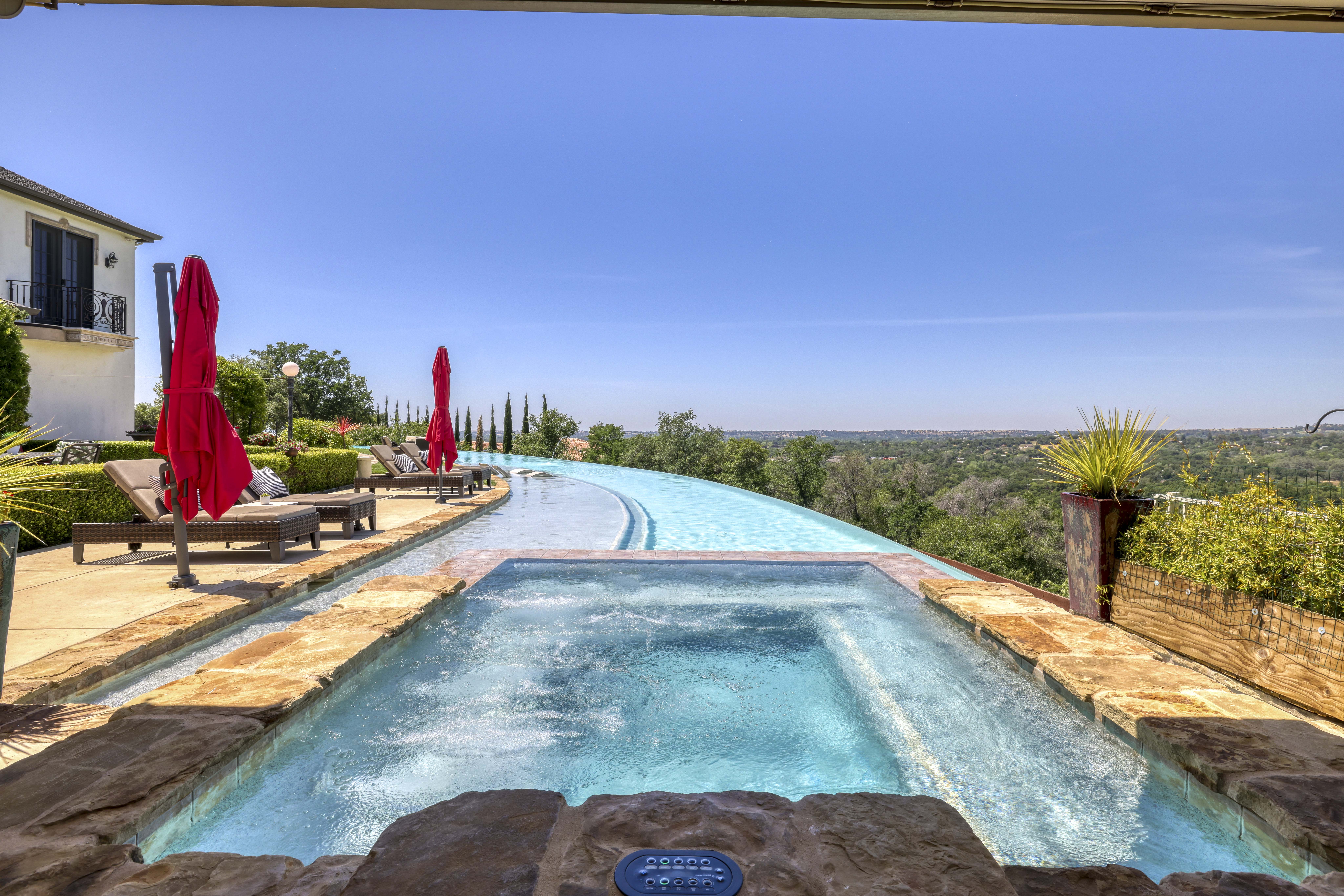 Raised spa with ledgerstone that is spilling over into to a long curved infinity edge pool during the day.
