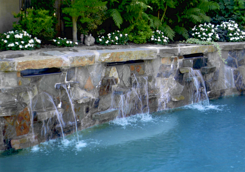 Pool with a raised wall with stone and three water features.