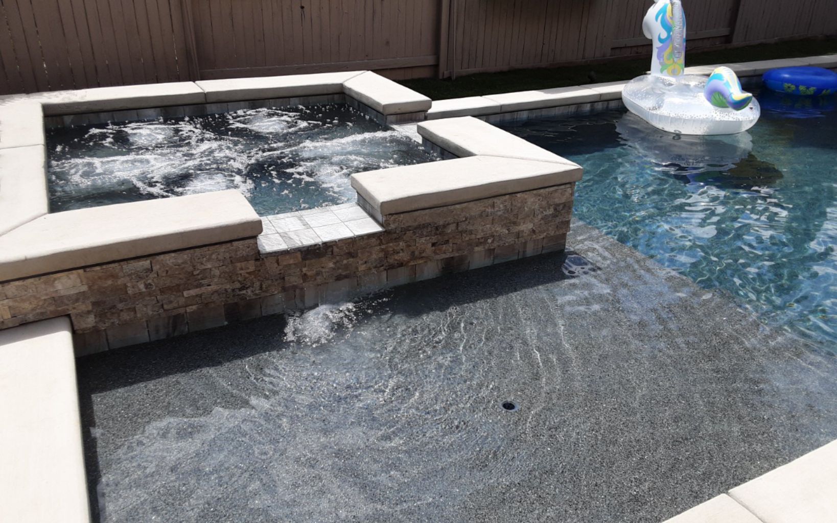Raised spa with ledgerstone and two spillovers, Cabo shelf and large unicorn pool float in attached pool.