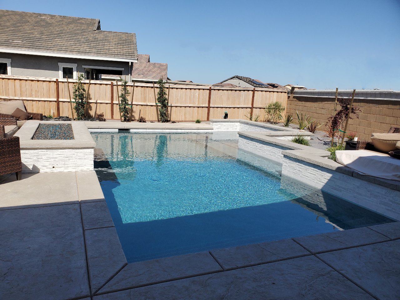 Custom shaped pool with raised wall with a large Cabo shelf and raised fire pit