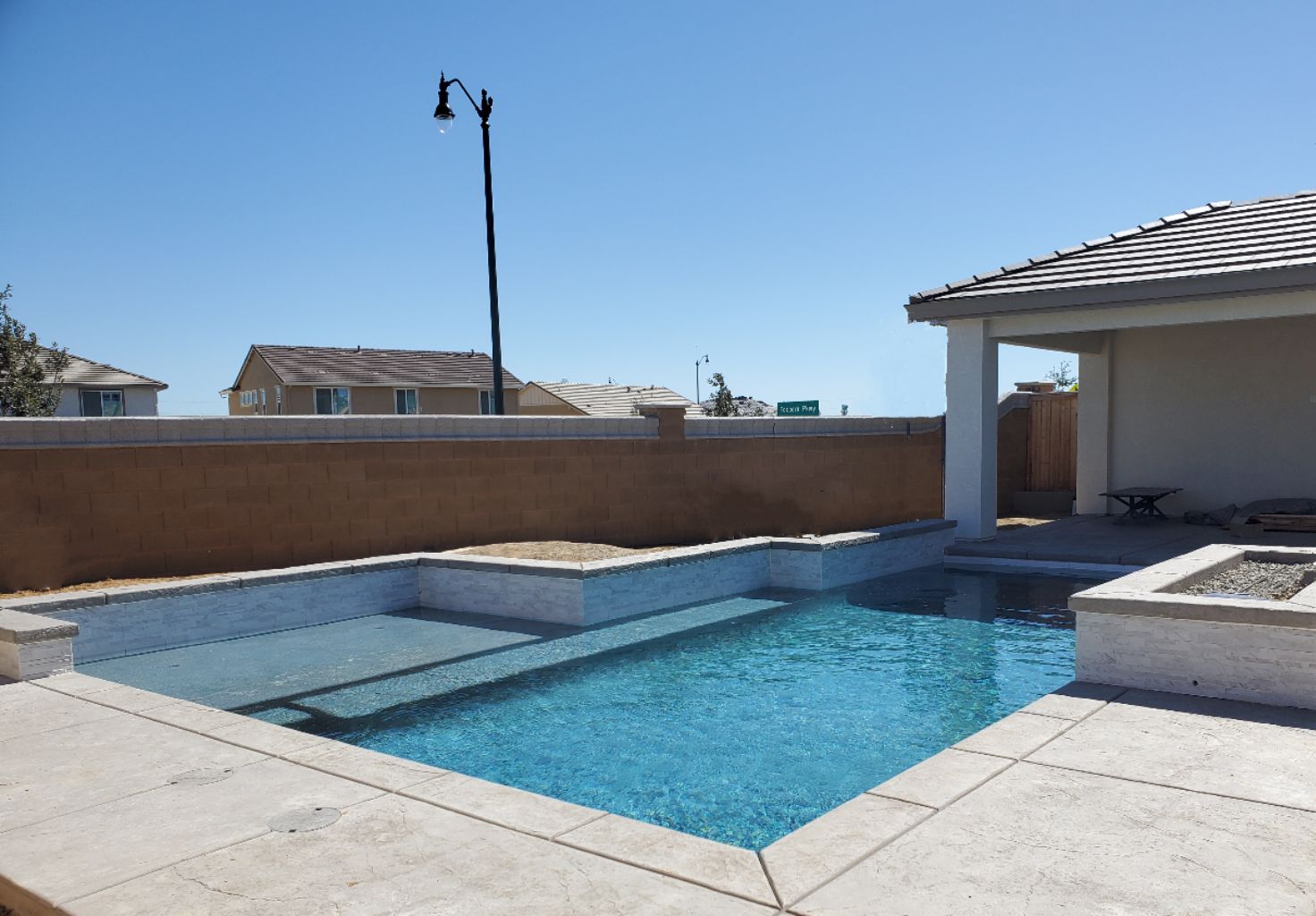 Custom shaped pool with raised wall with a large Cabo shelf and raised fire pit.