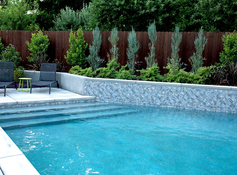 Custom shaped pool with a retaining wall for planters and long entry steps