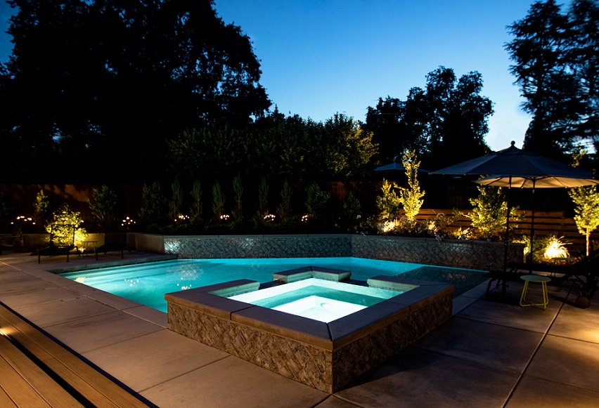 Custom shaped pool with Cabo shelf and raised spa with pool lights at dusk