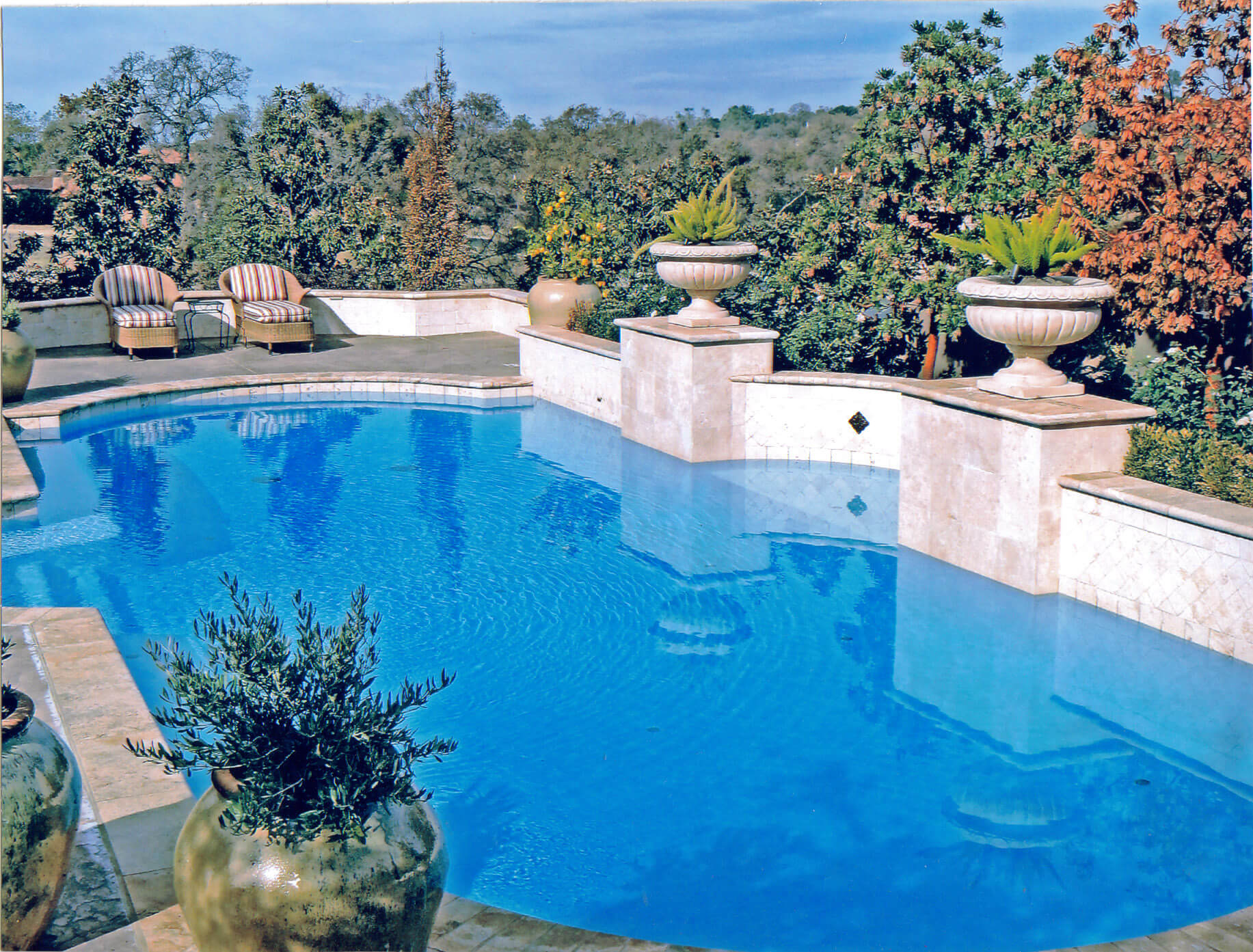 Custom shaped pool with a large raised wall with columns and planter bowls.