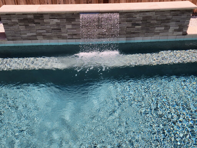 Raised ledgerstone faced wall with one sheer descent water feature and a concrete cap.