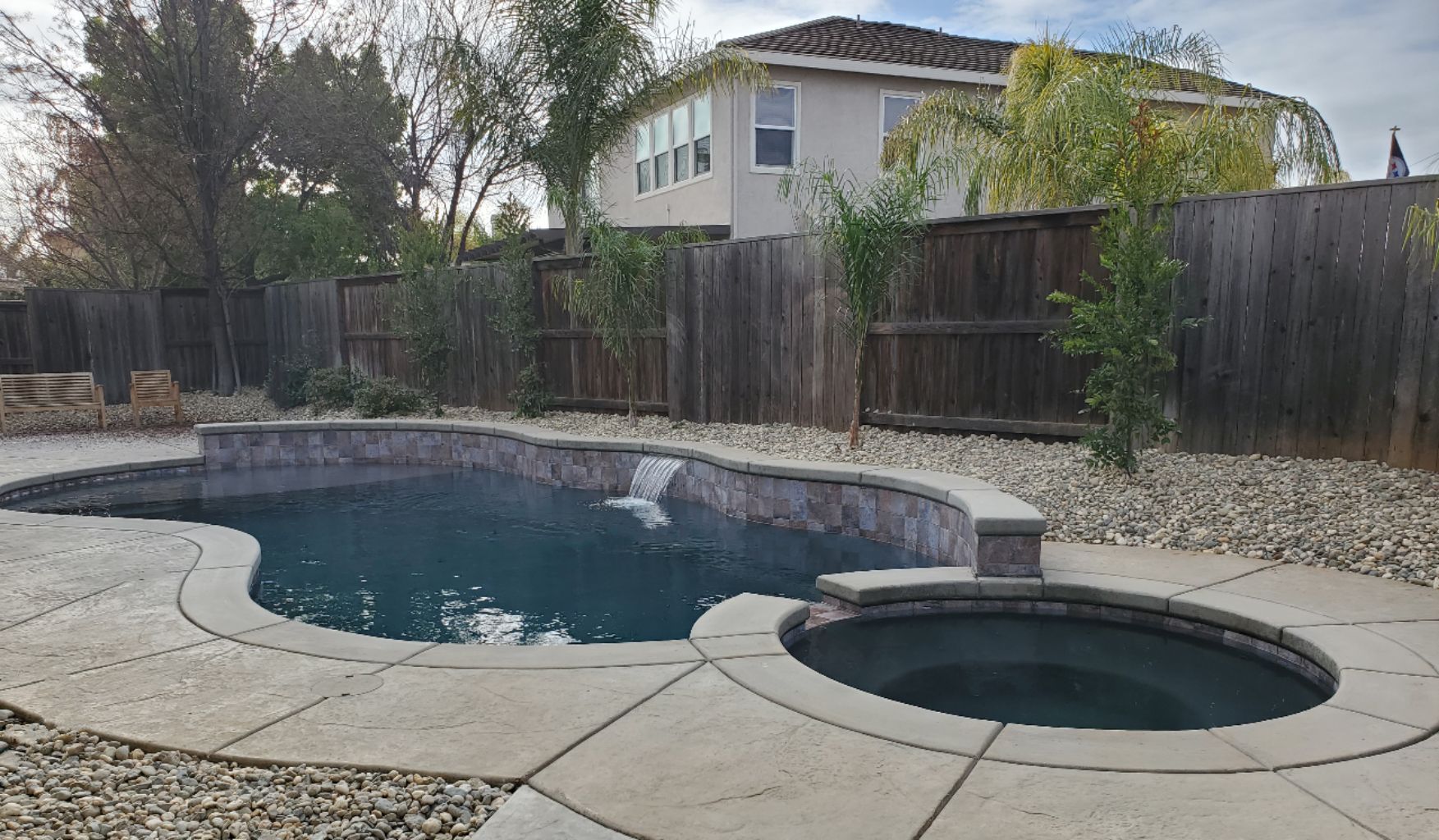 Freeform shaped pool with raised wall with sheer descent water feature and spa.