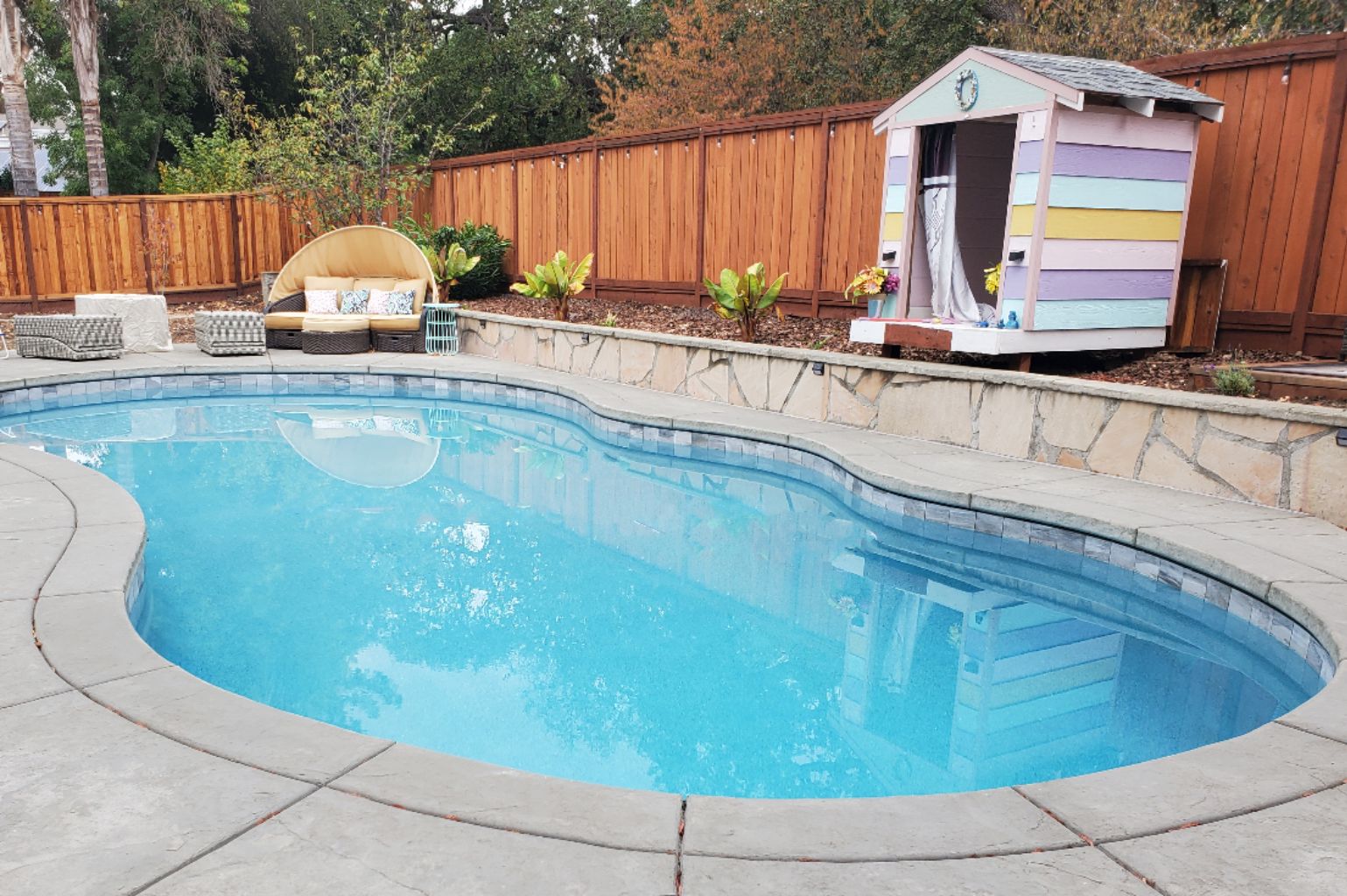 Freeform shaped pool with a colorful painted kid's playhouse.