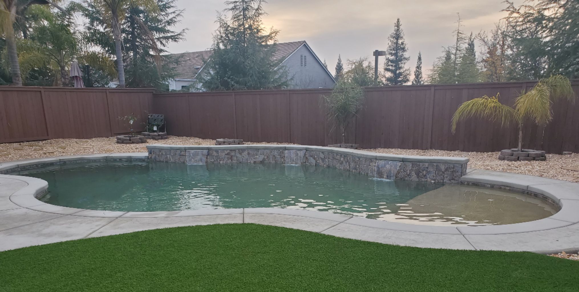 Freeform shaped pool with raised wall with three sheer descent water features and a large Cabo shelf.
