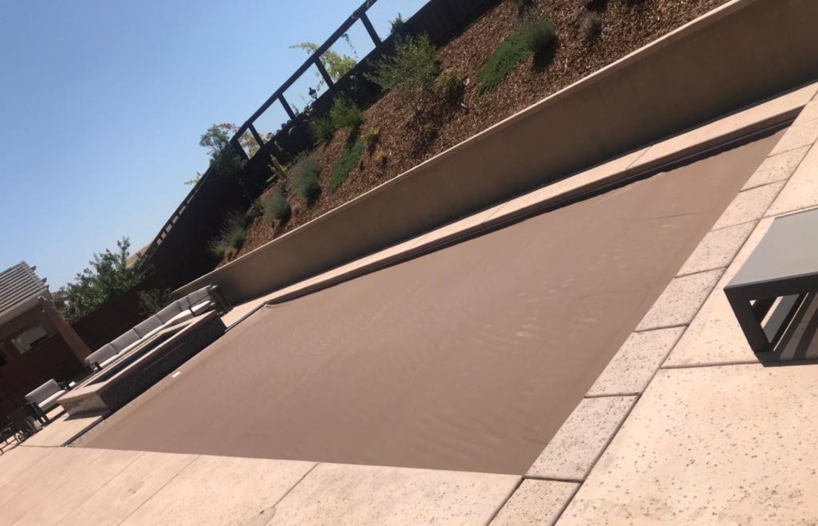 Rectangular shaped pool with a closed automatic pool cover in light brown and a seperate raised spa.