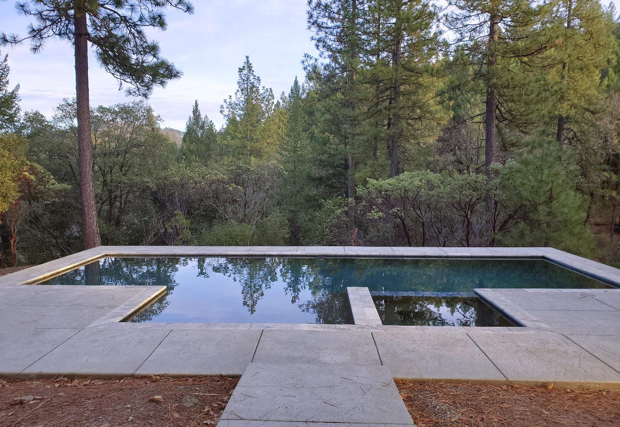 Rectangular shaped pool with larged bumped out Cabo shelf and spa with views of pine trees on sloped lot in Northern California.