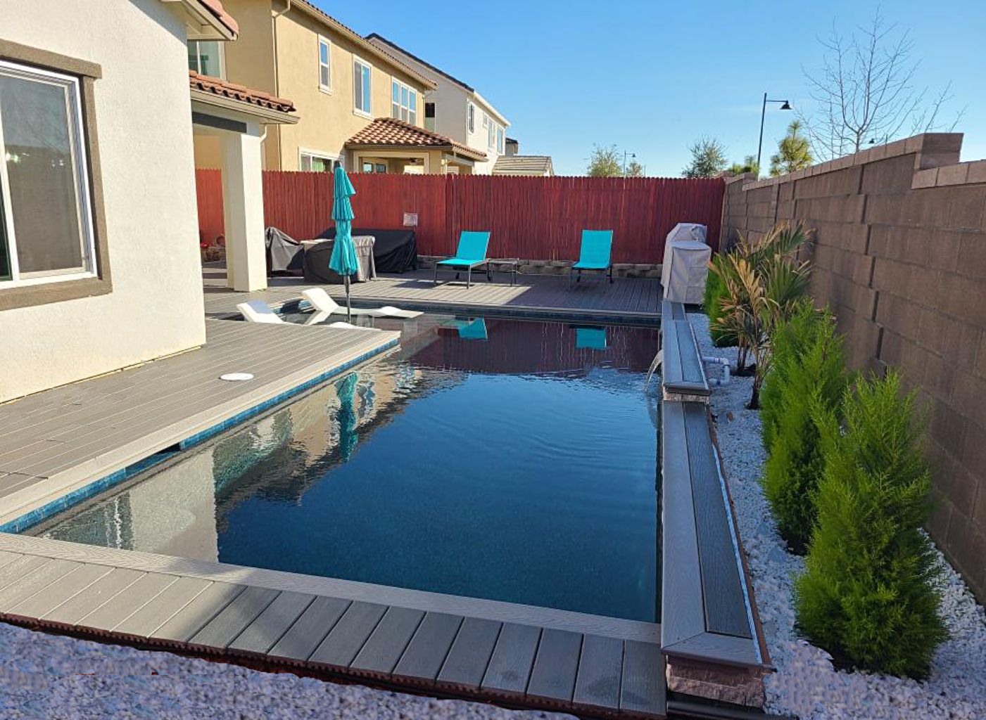 Rectangular shaped pool with a bumped out Cabo shelf with an umbrella and chaise lounges and Trex decking and coping.