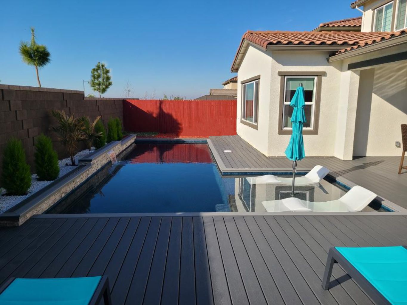 Rectangular shaped pool with a bumped out Cabo shelf with an umbrella and chaise lounges plus a raised wall with a sheer descent along with Trex decking and coping.