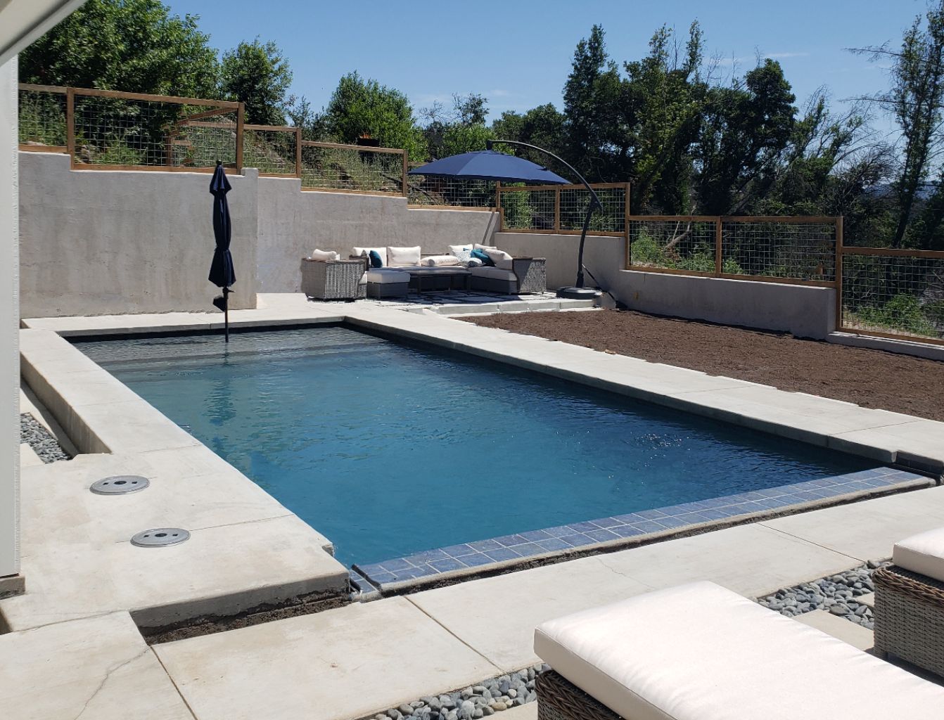 Rectangular pool with an automatic pool cover and large seating area and retaining walls.