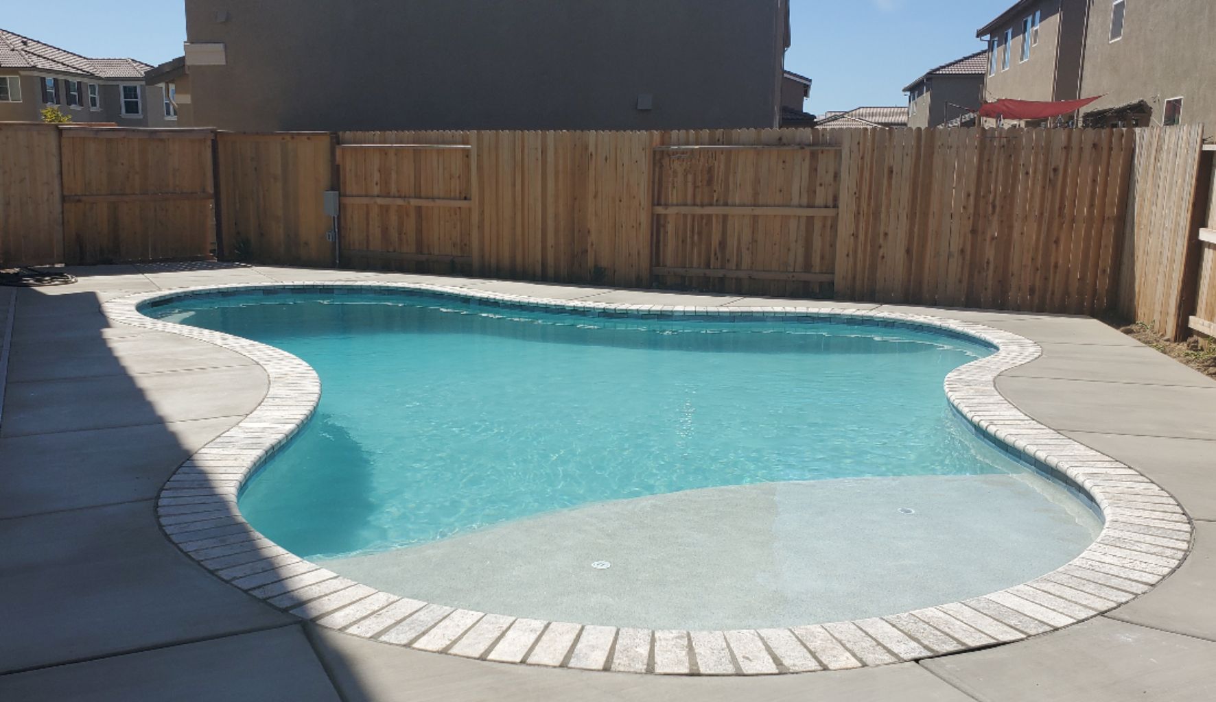 Freeform shaped pool with travertine coping and large Cabo shelf.