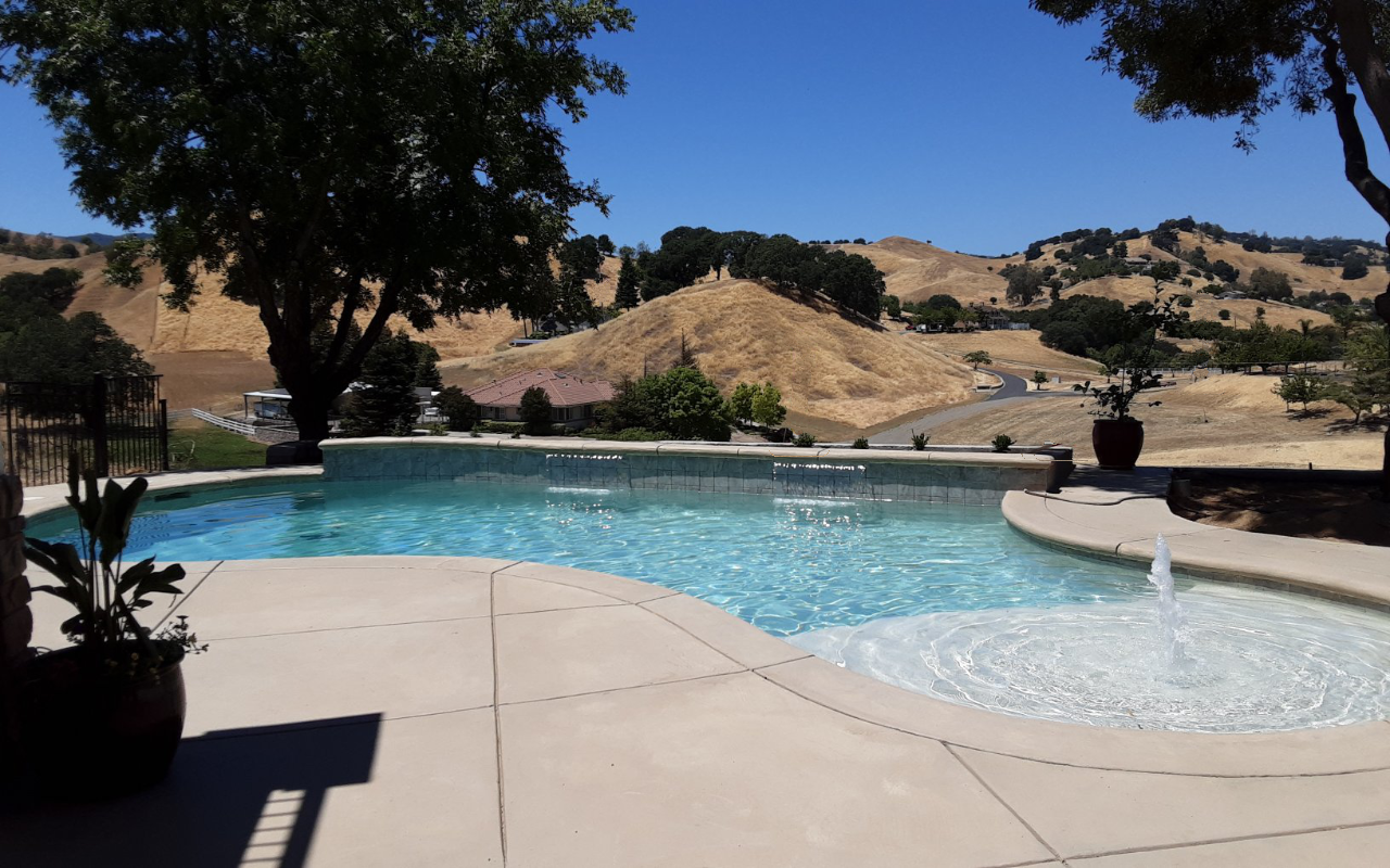 Freeform shaped pool with raised wall with two sheer descent water features and a large Cabo shelf with a bubbler.
