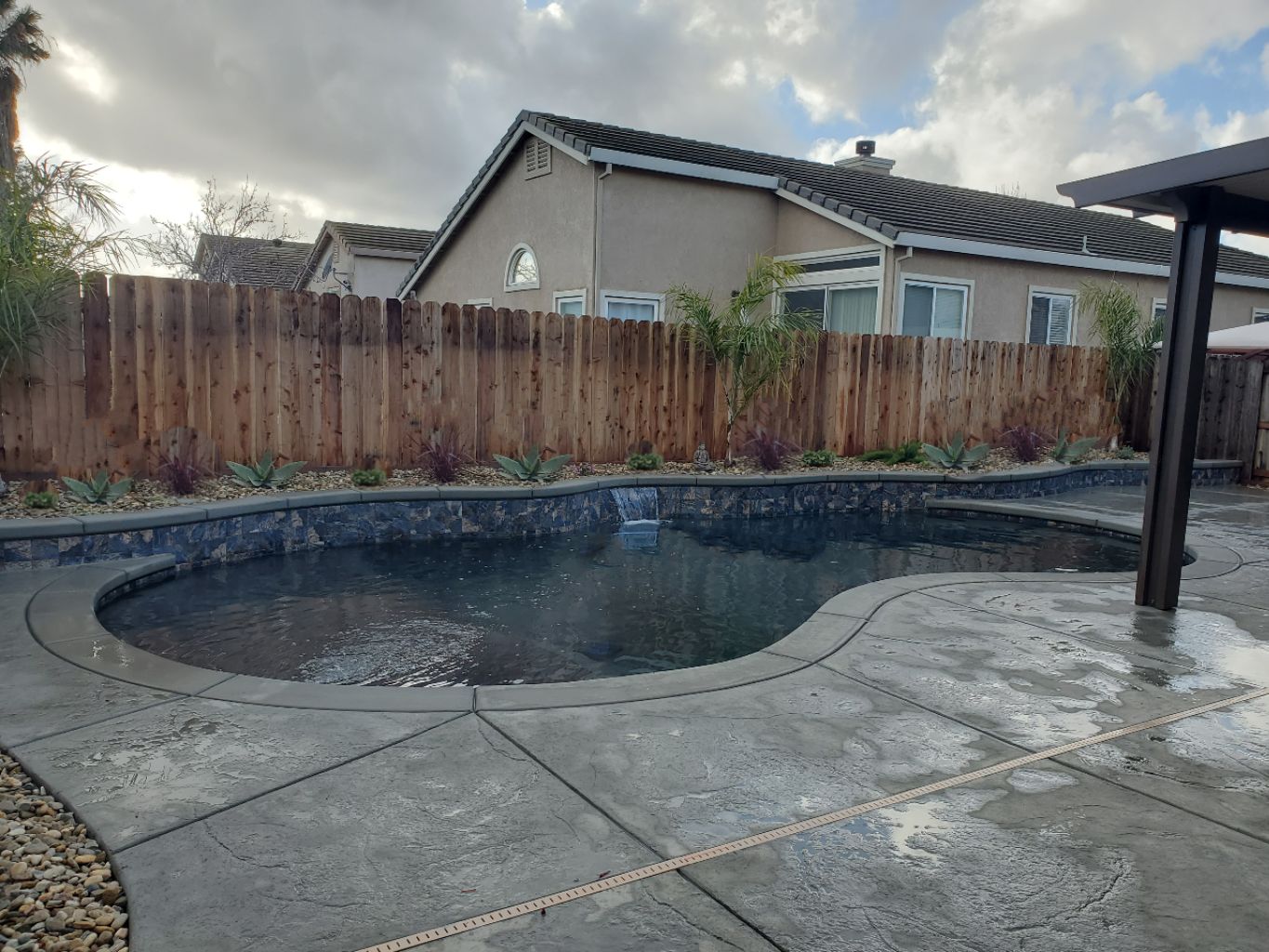 Freeform shaped pool with raised wall with sheer descent water feature.