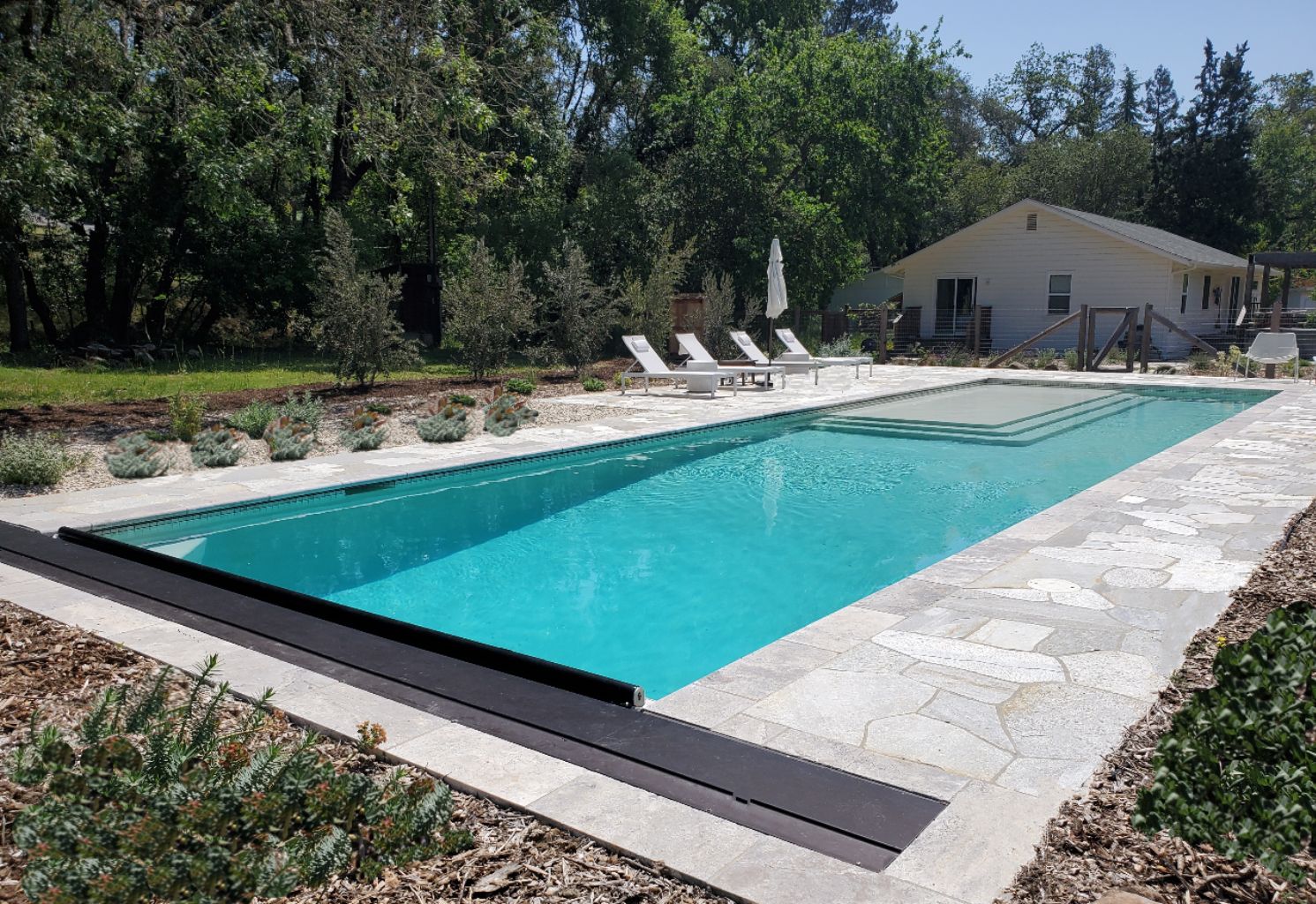 Rectangular shaped pool with turquoise blue water and a large Cabo shelf and automatic pool cover with an aluminum lid and flagstone decking.