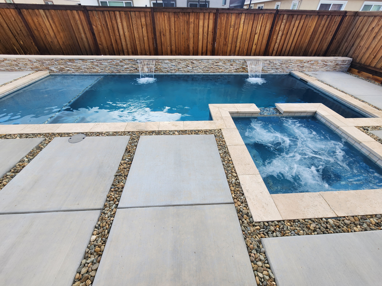 Rectangular shaped pool and spa and raised wall with two sheer descent water features and travertine stone coping.