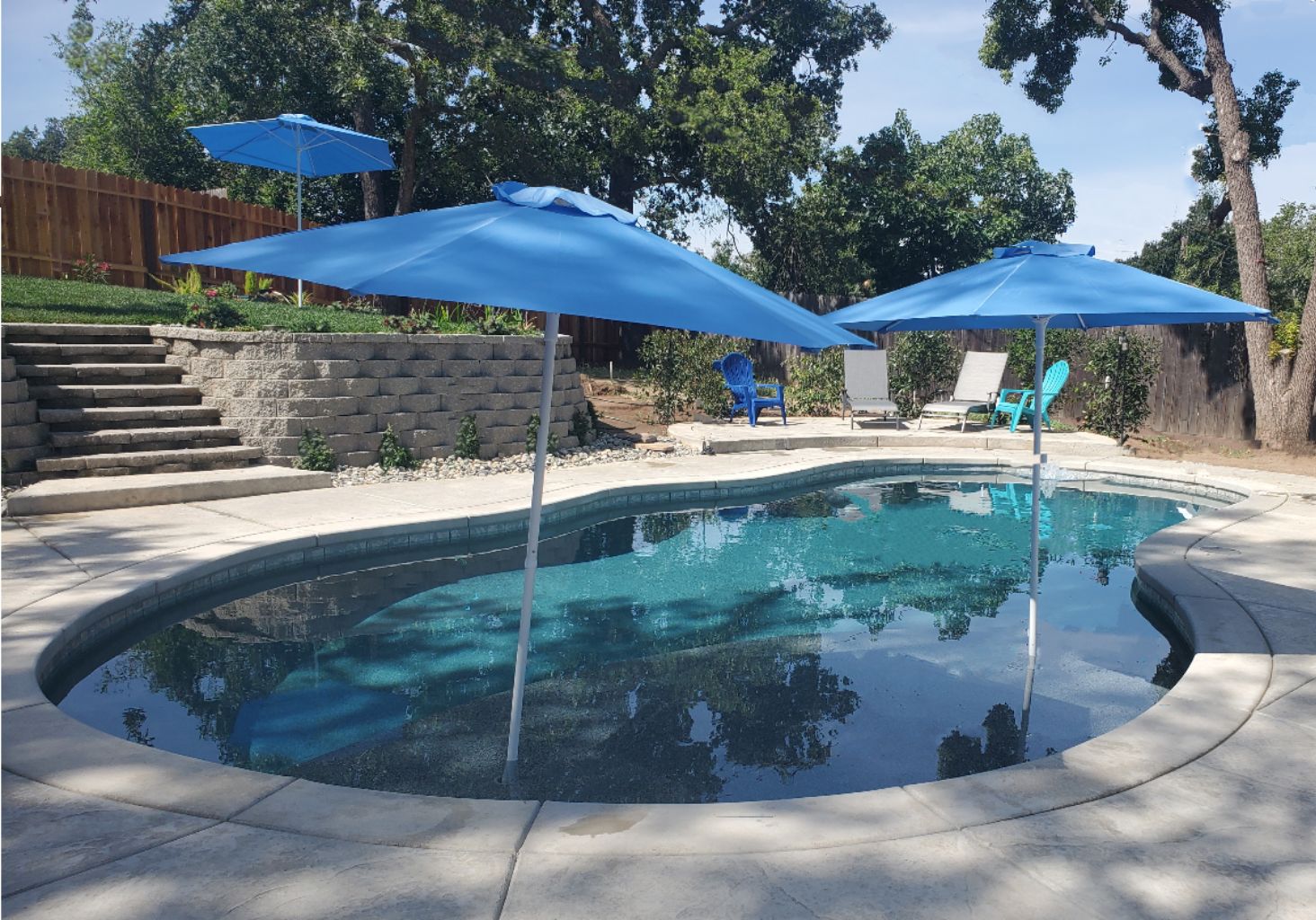 Freeform shaped pool with a large Cabo shelf with two umbrellas.