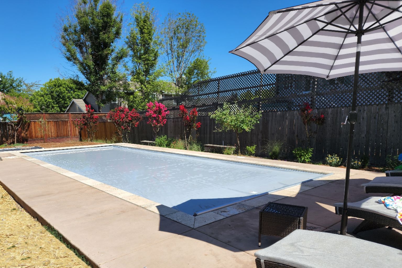 Rectangular shaped pool with an closed light gray automatic pool cover, stone coping and colored concrete decking.