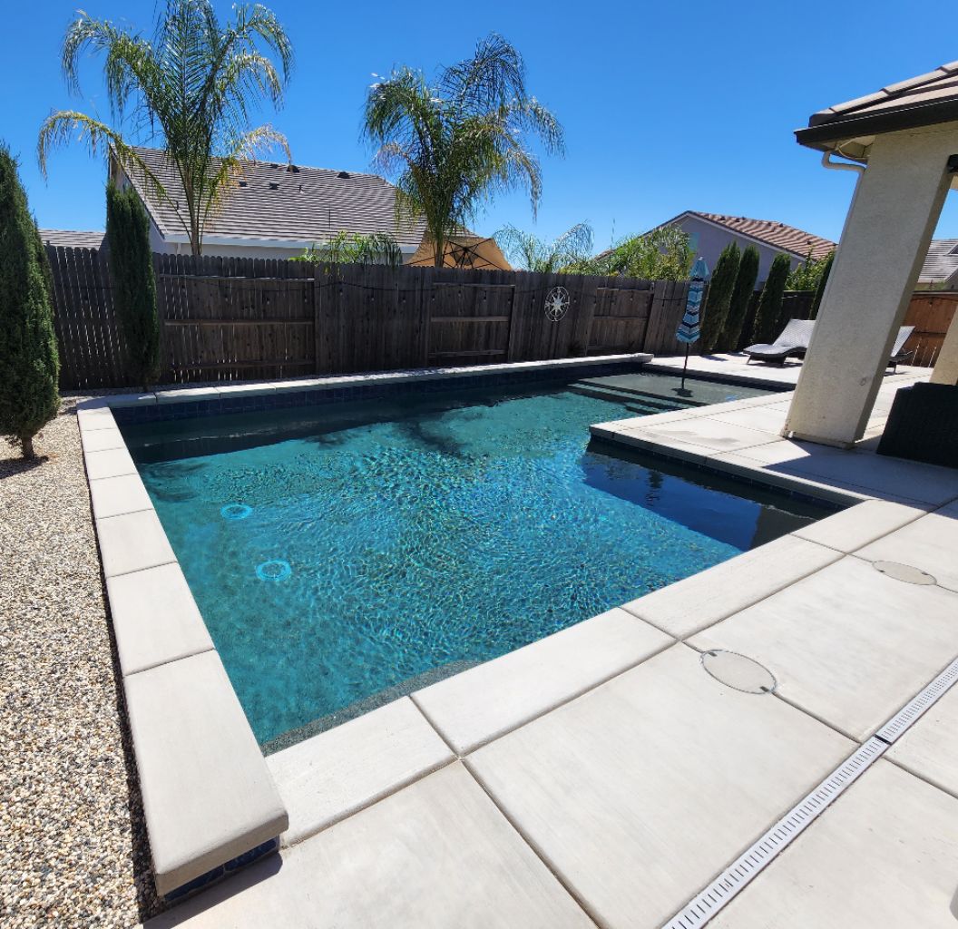 L-shaped custom pool with a Cabo shelf and concrete coping and decking.