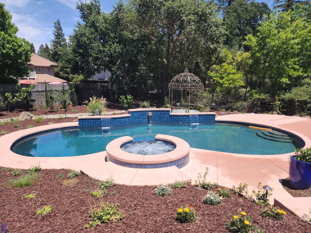 Freeform shaped pool with raised tiered wall and two sheer descent and one lion head water features and a raised spa.