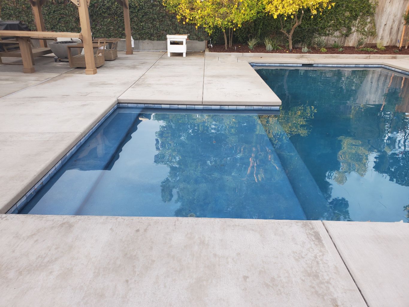 Rectangular shaped pool with larged bumped out Cabo shelf and concrete decking and coverred loggia with fire pit.
