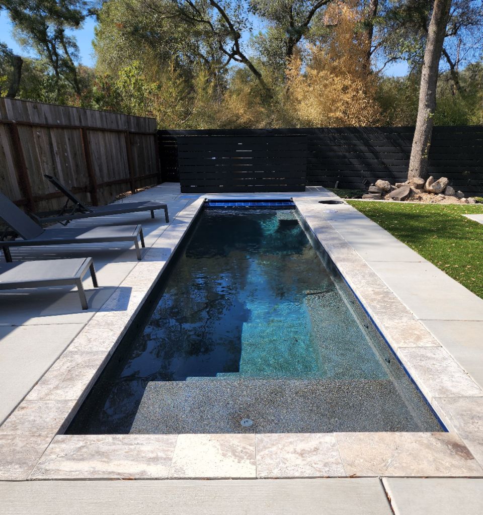 Small lap pool 27' x 7' with an automatic pool cover and travertine stone coping and concrete decking and turf.