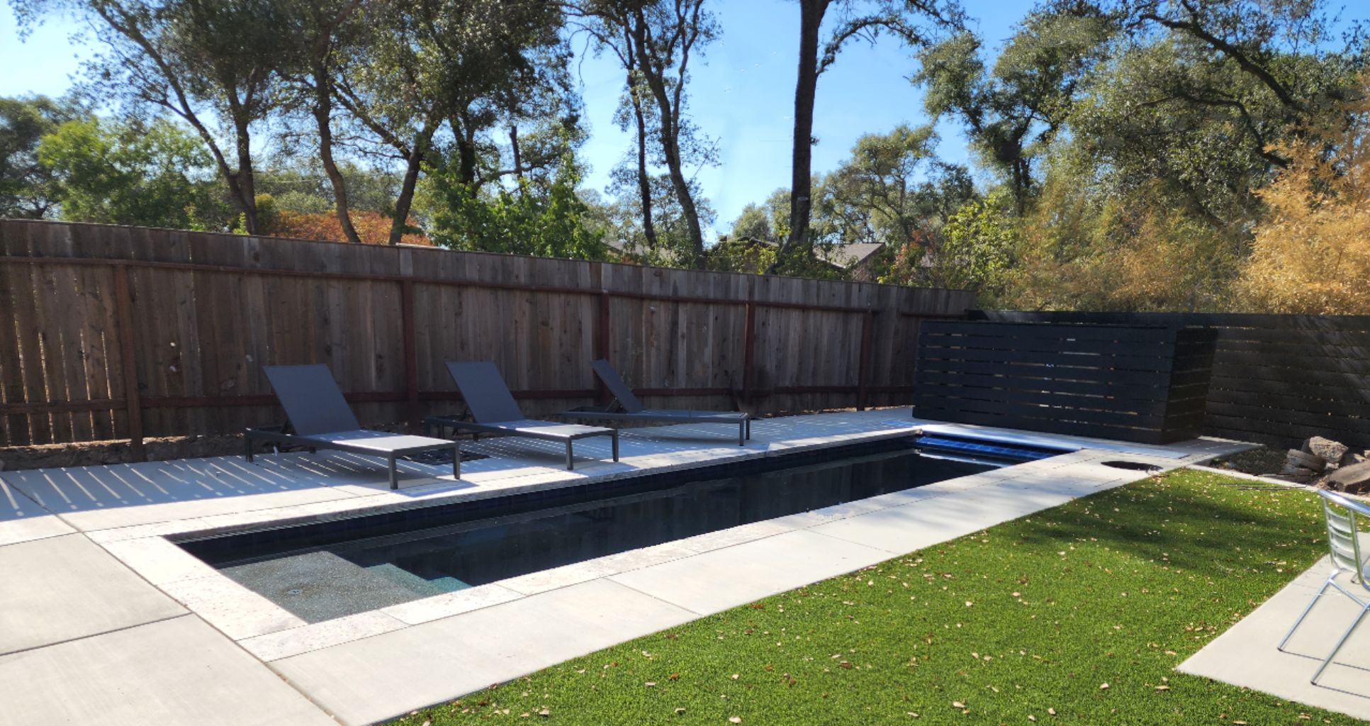 Small lap pool 27' x 7' with an automatic pool cover wtih an aluminum lid and travertine stone coping and concrete decking and turf in Granite Bay.