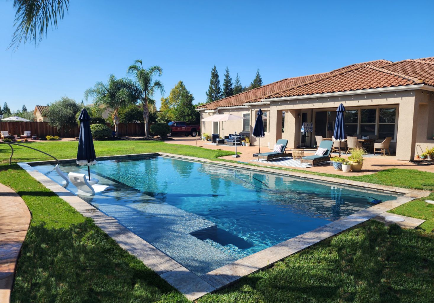 Rectangular shaped pool with a large Cabo shelf and travertine stone coping and grass around the pool.